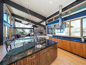 Kitchen featuring dark stone counters, vaulted ceiling with beams, plenty of natural light, and decorative light fixtures