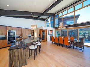 Dining space featuring high vaulted ceiling, light hardwood / wood-style floors, a chandelier, and beamed ceiling