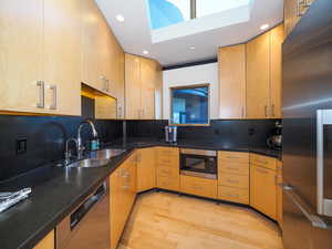 Kitchen with decorative backsplash, black microwave, a skylight, light wood-type flooring, and stainless steel fridge