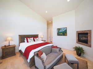 Bedroom with hardwood / wood-style flooring, high vaulted ceiling, and a premium fireplace