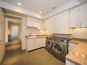 Clothes washing area featuring sink, washing machine and dryer, and cabinets