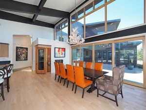 Dining area with a towering ceiling, beamed ceiling, light hardwood / wood-style floors, and a chandelier