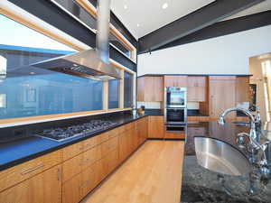 Kitchen featuring light hardwood / wood-style floors, wall chimney exhaust hood, sink, stainless steel double oven, and black gas stovetop