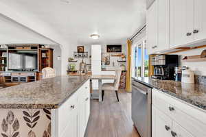 Kitchen featuring stainless steel dishwasher, light LVP flooring, white cabinetry, and dark stone counters