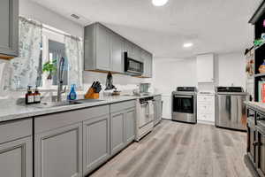 Kitchen with stainless steel range oven, white range with electric stovetop, gray cabinets, and light LVP floors and solo laundry room for the house