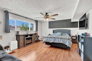 Bedroom with light LVP floors, ceiling fan, and a textured ceiling