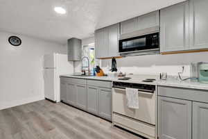 Kitchen with light LVP flooring, electric stove, gray cabinetry, sink, and a textured ceiling