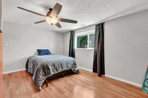 Bedroom with light LVP  floors, ceiling fan, and a textured ceiling