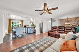 Living room with ceiling fan, wooden accent walls, a textured ceiling, and LVP flooring