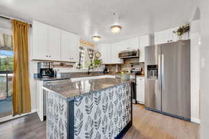 Kitchen with stainless steel appliances, light LVP floors, white cabinetry, a kitchen island, and dark stone countertops