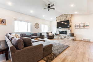 Living room with ceiling fan, a fireplace, light hardwood / LVP-style flooring, and lofted ceiling