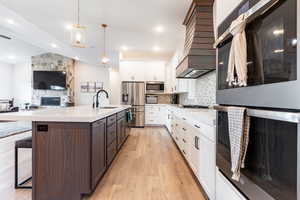 Kitchen with sink, a fireplace, appliances with stainless steel finishes, light hardwood / wood-style flooring, and white cabinetry