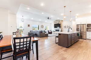 Kitchen featuring a stone fireplace, appliances with stainless steel finishes, dark brown cabinets, light hardwood / wood-style floors, and a center island with sink