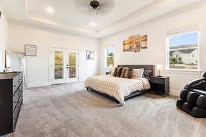 Primary Bedroom featuring ceiling fan, a raised ceiling, access to outside, light colored carpet, and french doors