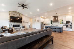 Living room with sink, a fireplace, light hardwood / wood-style flooring, ceiling fan, and lofted ceiling