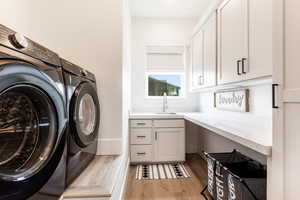 Washroom with sink, washing machine and dryer, cabinets, and light wood-type flooring