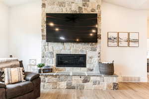 Living room featuring hardwood / wood-style flooring, lofted ceiling, and a stone fireplace