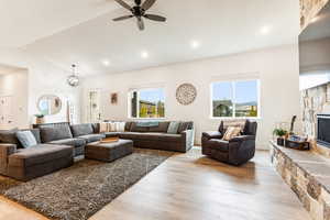 Living room featuring a fireplace, light hardwood / wood-style flooring, ceiling fan, and lofted ceiling