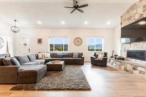 Living room featuring light hardwood / wood-style flooring, ceiling fan with notable chandelier, and a stone fireplace