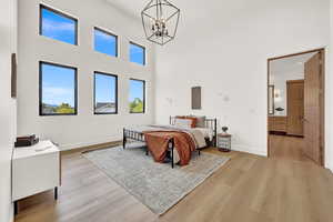 Bedroom featuring a towering ceiling, a chandelier, and light wood-type flooring