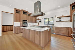 Kitchen featuring tasteful backsplash, appliances with stainless steel finishes, island exhaust hood, a center island, and light hardwood / wood-style flooring