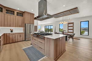 Kitchen with appliances with stainless steel finishes, wall chimney exhaust hood, hanging light fixtures, and light wood-type flooring