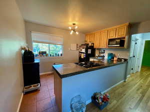 Kitchen with a chandelier, black appliances, light brown cabinets, light wood-type flooring, and kitchen peninsula