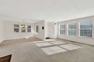 Unfurnished living room with light carpet, a chandelier, and plenty of natural light