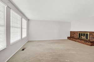 Unfurnished living room with light colored carpet and a brick fireplace