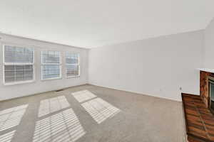 Unfurnished living room with carpet flooring and a brick fireplace