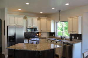 Kitchen featuring appliances with stainless steel finishes, decorative backsplash, sink, light stone counters, and a kitchen island