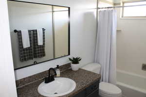 Full bathroom with vanity, shower / bath combo, and toilet