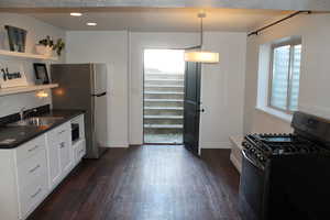 Kitchen with dark hardwood / wood-style flooring, gas range, white cabinetry, sink, and decorative light fixtures