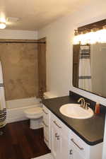 Full bathroom featuring vanity, a textured ceiling, wood-type flooring, shower / bath combination with curtain, and toilet