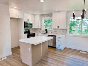 Kitchen with stainless steel appliances, white cabinets, decorative light fixtures, and light wood-type flooring