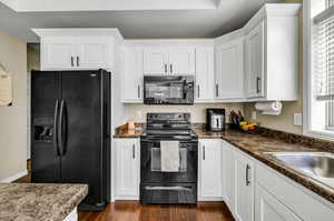 Kitchen with dark wood-type flooring, white cabinetry, dark stone countertops, and black appliances