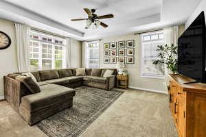 Living room with ceiling fan, a raised ceiling, plenty of natural light, and light colored carpet