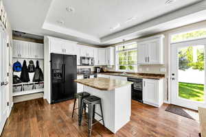 Kitchen with dark hardwood / wood-style flooring, black appliances, and white cabinetry