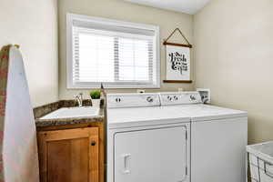 Clothes washing area with sink, washer and clothes dryer, and cabinets