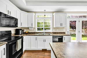 Kitchen with sink, hardwood / wood-style floors, black appliances, and a wealth of natural light