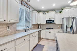 Kitchen with light wood-type flooring, stainless steel appliances, tasteful backsplash, and white cabinets