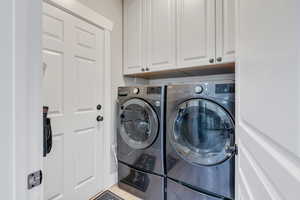 Clothes washing area with light wood-type flooring, cabinets, and washer and clothes dryer