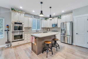 Kitchen featuring a kitchen bar, decorative light fixtures, decorative backsplash, light hardwood / wood-style floors, and stainless steel appliances