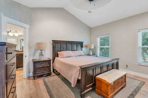 Bedroom featuring light hardwood / wood-style floors, vaulted ceiling, connected bathroom, and multiple windows