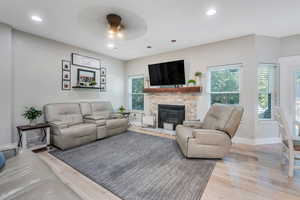 Living room featuring ceiling fan, a stone fireplace, and light hardwood / wood-style flooring