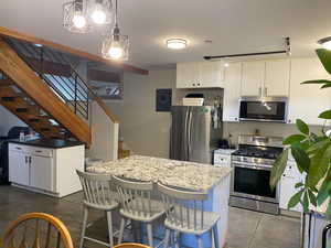 Kitchen featuring white cabinets, tile patterned flooring, pendant lighting, and stainless steel appliances