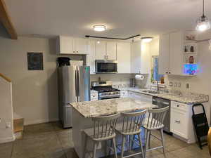 Kitchen featuring white cabinets, sink, dark tile patterned flooring, a center island, and stainless steel appliances