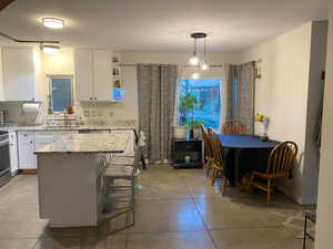 Kitchen with white cabinets, a kitchen bar, light stone counters, light tile patterned floors, and a center island