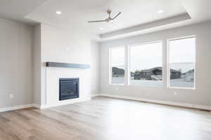 Unfurnished living room featuring a raised ceiling, a fireplace, light wood-type flooring, and ceiling fan