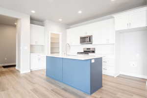 Kitchen with light hardwood / wood-style floors, appliances with stainless steel finishes, white cabinets, and an island with sink